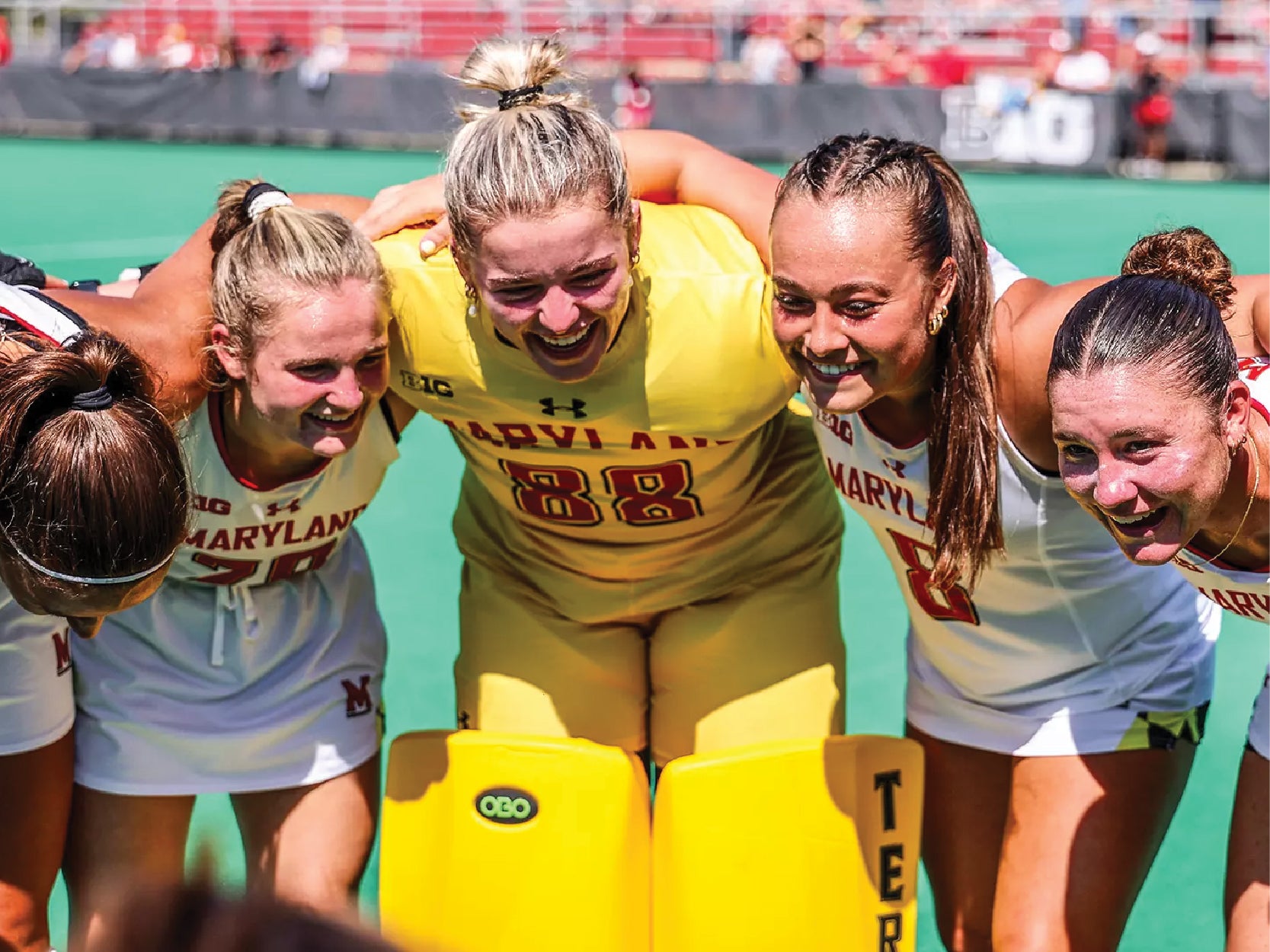 Five members of the UMD field hockey team smile and laugh while linking arms
