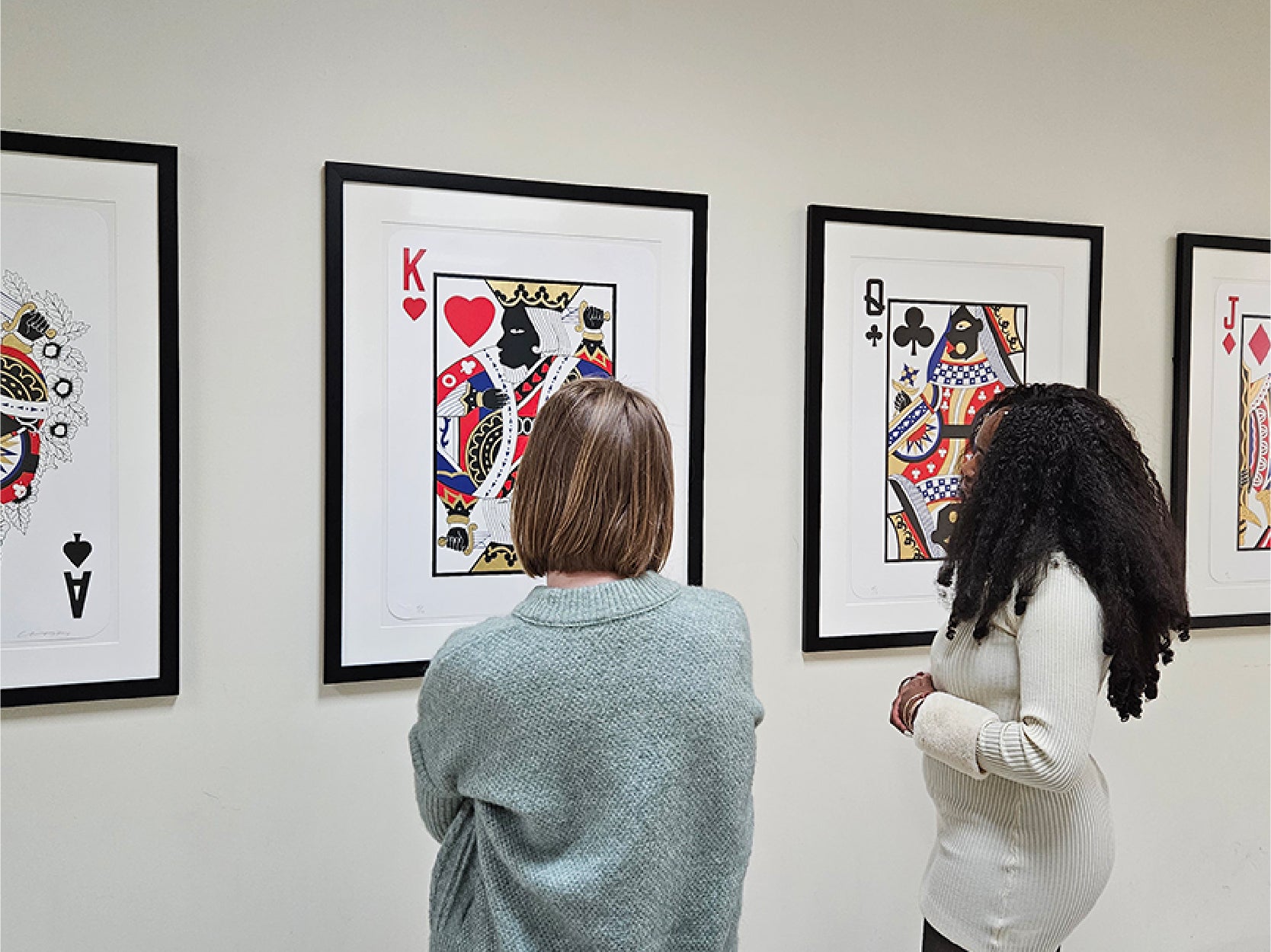 Two women look at a series of framed art pieces on the wall of STAMP