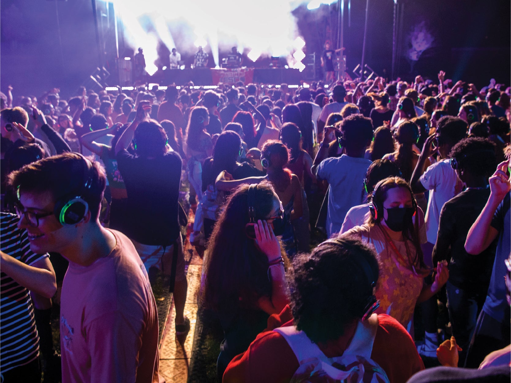 A large crowd of UMD students dances while wearing headphones in front of a stage.