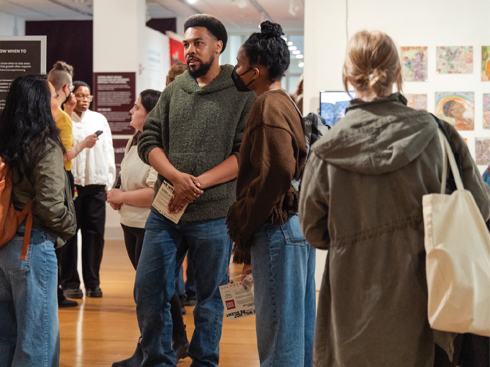 A group of people take in art and converse in the STAMP Gallery