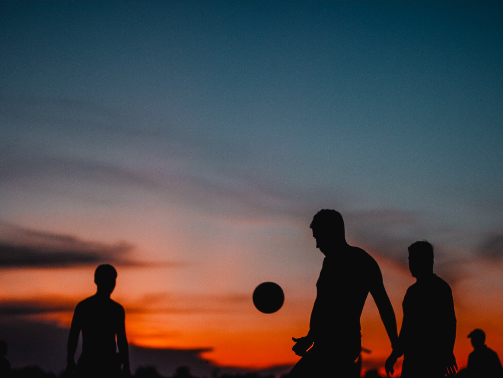 An image of three silhouettes playing with a ball with a sunset background