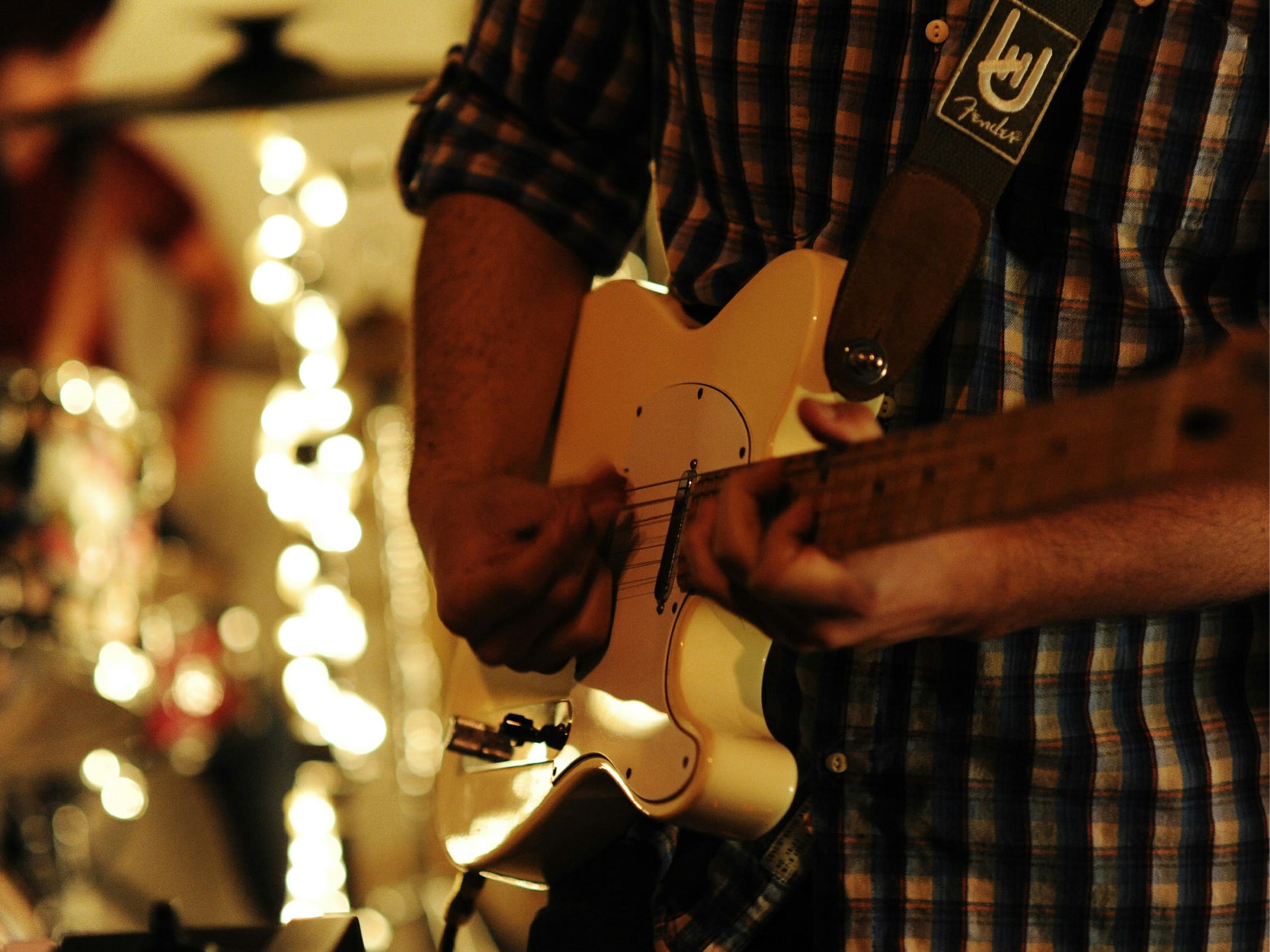 A photo of a man playing a white electric guitar. The photo is zoomed in on the guitar and only shoing the mid section of the man.